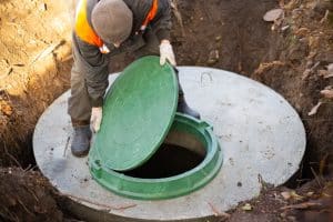 A worker installs a sewer manhole on a septic tank made of concrete rings. Construction of sewerage networks for country houses.